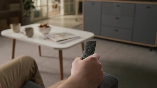 Hand eines männlichen Zuschauers, der den Fernsehkanal mit Fernbedienung wechselt