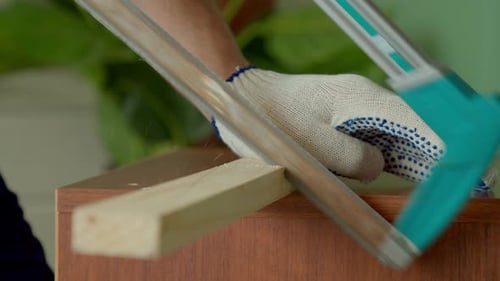Plan rapproché d'un charpentier mâle coupant une planche de bois avec une scie à main à l'intérieur