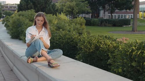 Woman Writing in Notebook Outdoors in Urban Park
