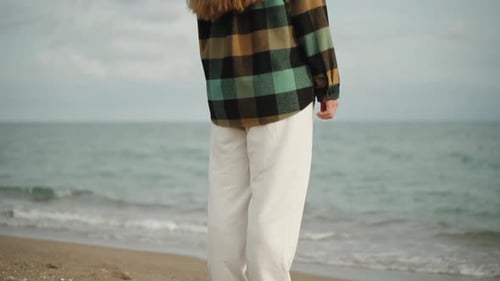 a young woman in a plaid shirt and white pants on a sea beach looks into the distance, slowed down f