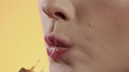 woman taking a bite of a bar, close-up biting of snack on yellow background