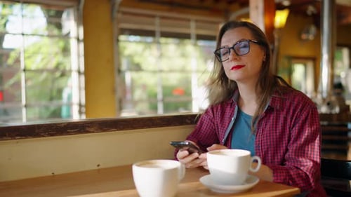 Woman is Using Smartphone and Drinking Coffee in the Cafe