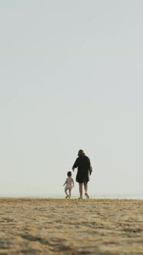 A Mother and Young Child Joyfully Walking Together on the Beautiful Beach at Sunset Vertical Video
