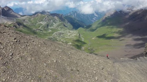 Aerial shot of a man running fast down the ridge on the steep and sharp edge of the bare and rocky s