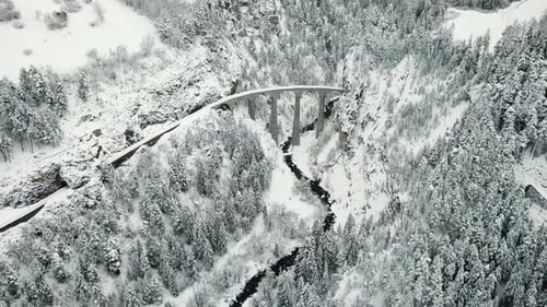 Drone view of the Landwasser Viaduct, a stunning railway bridge amidst a snowy forest landscape, fly