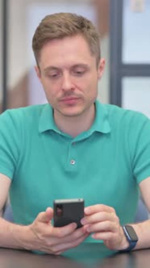 Man in teal polo shirt uses cell phone indoors