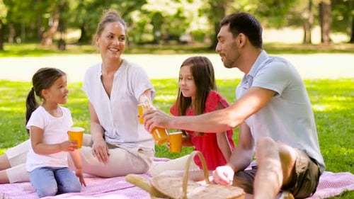 Happy hispanic family enjoying summer picnic with orange juice in the park