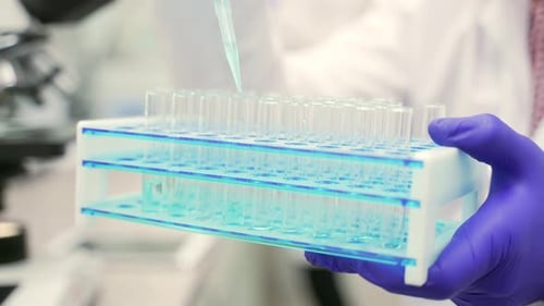Close up of scientists researcher hands with protective gloves dropping the chemical liquid solution