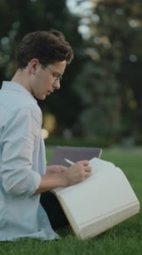 Young Man Writing in Notebook While Working Remotely in a Park