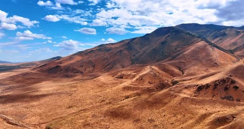 Flight over the deserted rocky landscape on sunny day. Clouds covering the sky shade the mountains.