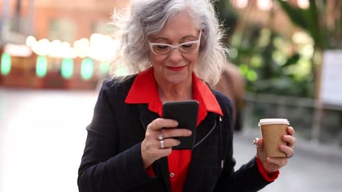 mature woman with gray hair, with coffee and smart phone outdoors