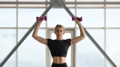 Mujer rubia levantando mancuernas durante un entrenamiento intenso y poderoso
