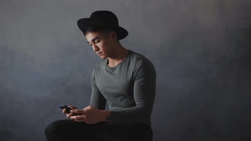 Young Asian Man in Casual Attire Using Smartphone in Studio Setting