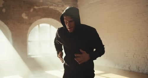 Um homem com roupas esportivas com capuz corre para se manter em uma academia ensolarada. Atividades esportivas para melhorar