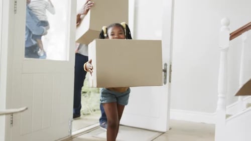 Glückliches afroamerikanisches Paar mit Sohn und Tochter, die Kisten ins Haus bringen, Zeitlupe