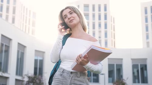 Smiling Woman with Books Talking on Cellphone Outside College
