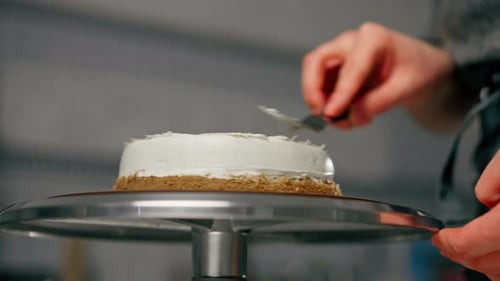 Close Up Female Baker in a Professional Close Up Kitchen Distributes Cream Onto Sponge Cake with a