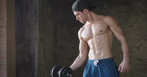A muscular and sweaty man is training at the gym by lifting the gym weights to strengthen his musc
