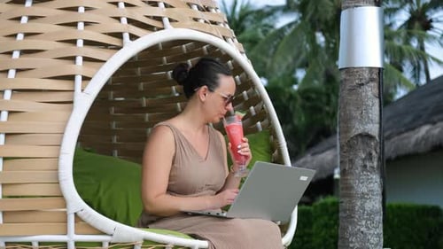 Woman Works on Laptop in Tropical Hanging Chair