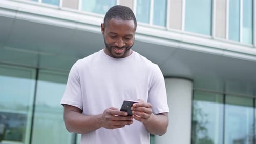 African American Man Holding Smartphone Touch Screen Typing Scroll Page on Urban Street in City Guy