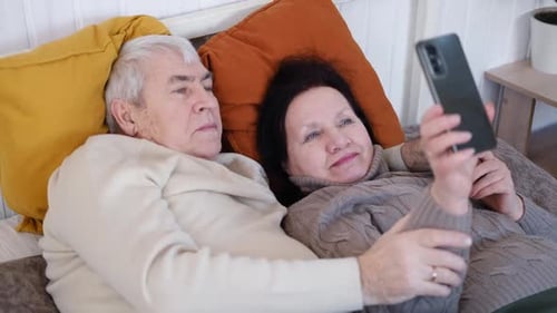Senior Couple Relaxing in Bed, Using Smartphone Together