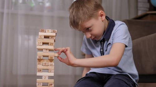 Ein aufgeregter Junge spielt ein Brettspiel mit Jenga. Er holt einen Holzblock heraus