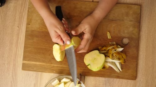 05 1Woman cutting fresh apple with knife on wooden board, placing slices into clear glass bowl for l