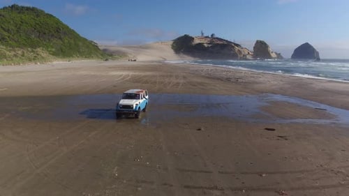 Friends cruise along sandy beach road in vintage suv aerial view