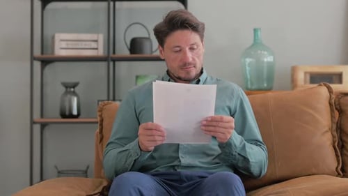 Adult Man Reads Documents on Comfortable Couch