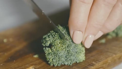 Detail of a green broccoli being picked up and cut in half with a knife, the broccoli is resting on