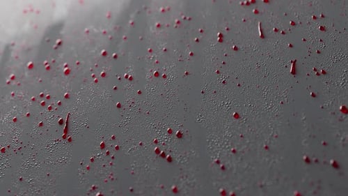 Las gotas viscosas rojas se deslizan lentamente por una superficie gris.