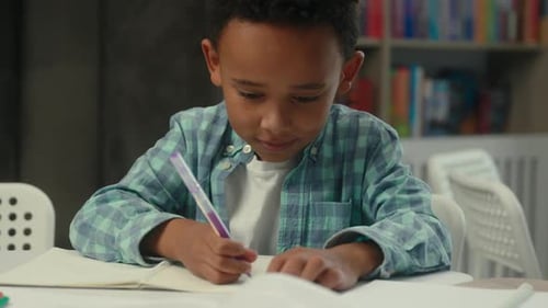 Boy Writing in Notebook at School Desk