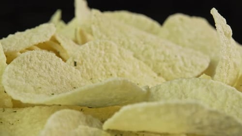 Close up potato chips rotate on black background. Snack for drinks. Golden fried potatoes. Crispy