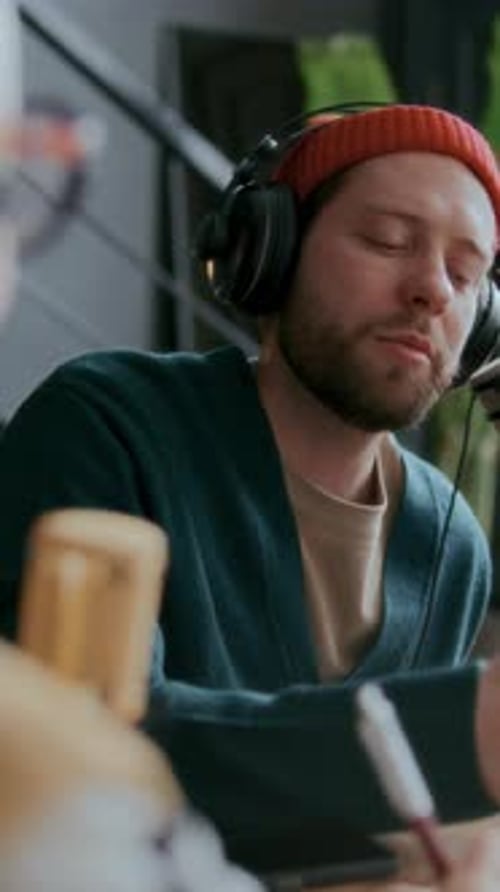 Vertical of Young Male Podcaster Interviewing Guest in Studio