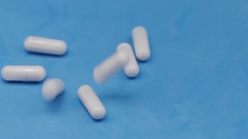 Slow motion video: white pills or capsules falling on a blue background.