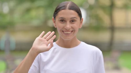 Begrüßende hispanische Frau, die winkt, um Hallo zu sagen, während sie im Freien steht