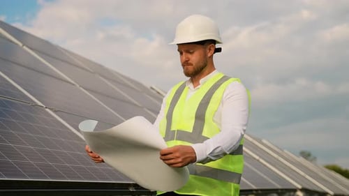 Engineer with Blueprint Inspecting Solar Panel Farm