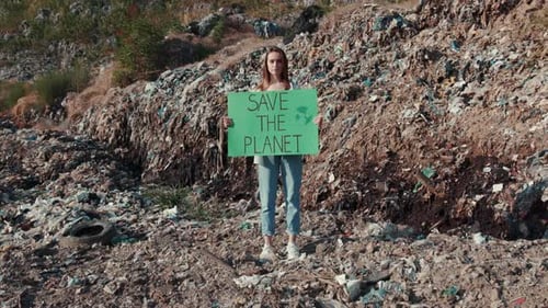 Young Woman Holding Sign in Garbage Dump