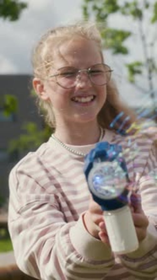 Cheerful Girls Playing with Toy Gun Blowing Stream of Soap Bubbles