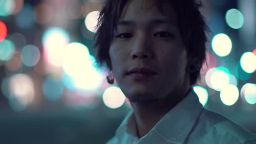 Portrait of the Young Handsome Asian Guy Looking at the Camera. In the Background Blurred Big City