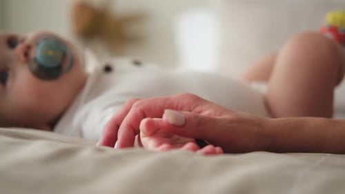 Baby Holding Adult Finger on Bed in Bright Room