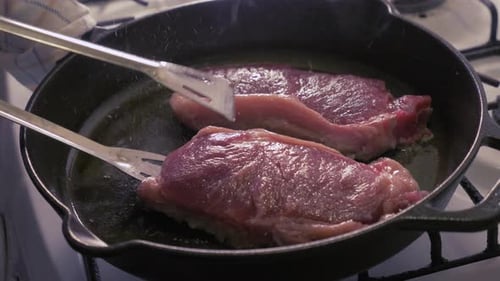 Steaks cuits et retournés dans une poêle en fonte avec de l'huile - Ralenti