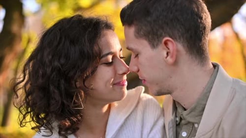 A romantic couple in an autumn park. Man kissing his woman. Autumn atmosphere, yellowed trees and le