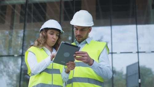 Man and Woman Engineers Have Conversation and using Tablet Computer on Construction Site. Glass Bui