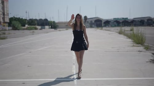 Jeune fille caucasienne en robe noire courte marchant face à la caméra dans une zone industrielle