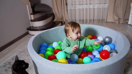 Excited baby boy clapping hands by the colorful toys in the basin he’s sitting in