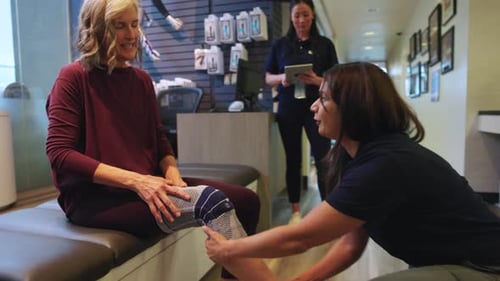 Physical Therapist Helping Senior Patient with Knee Sleeve in Clinic 3034 Years