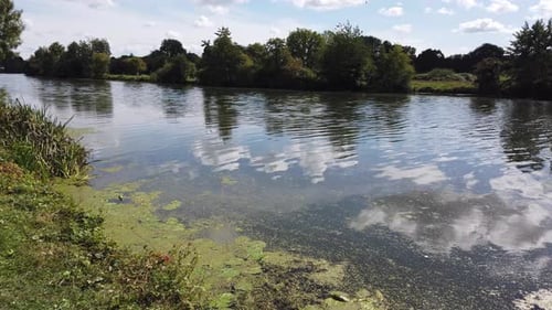 Plätschernde Reflexionen von Wolken und Himmel im langsam fließenden Fluss.