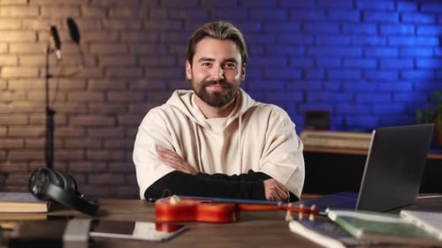 Smiling Man Sitting at Desk with Ukulele and Laptop