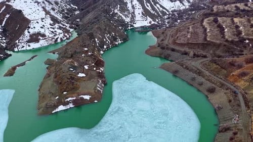 Drone Flight Over Mountain Lake with Floating Ice and Snowy Hills
